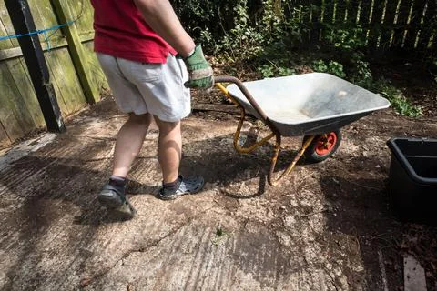 Empty wheel barrow in use in a garden yard by a man with his legs showing Stock Photos