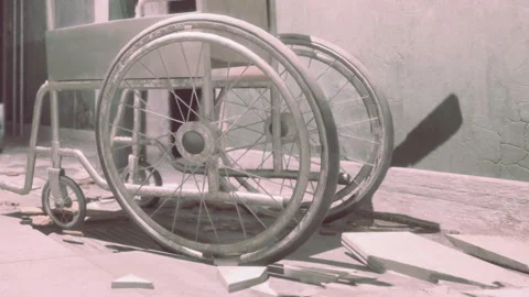 Empty wheelchair resting on cracked floor in abandoned room Stock Footage 342820589