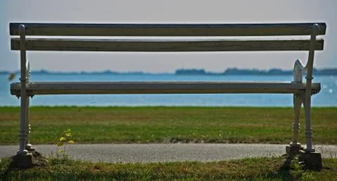 Empty white bench looking at grass field and lake in distance Stock Photos