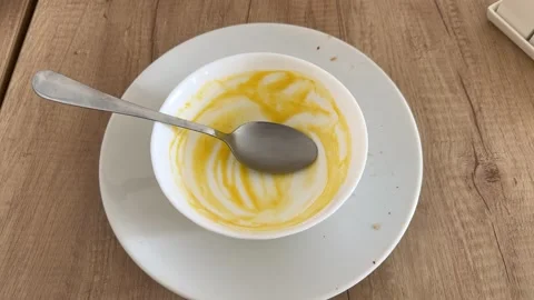 Empty white bowl with yellow soup residue and spoon on plate Video stock 343408016
