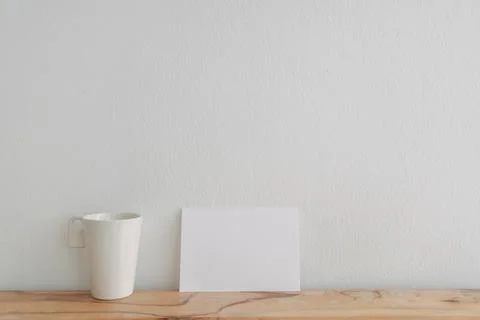 Empty white card mockup lean on a tea cup with white wall. Stock-Fotos