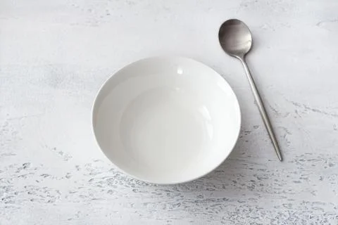 Empty white ceramic bowl with stainless steel spoon on light gray textured .. Stock Photos
