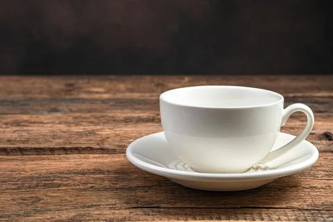 An empty white ceramic cup and saucer on a wooden brown background. Stock Photos