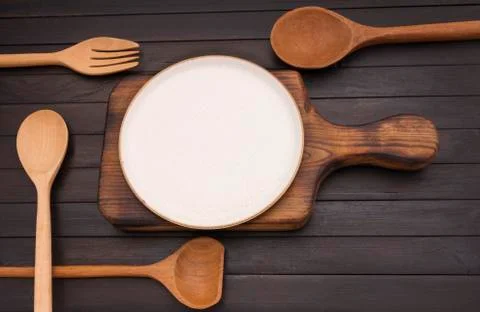 Empty white ceramic plate on an old wooden cutting board with spoon and fork  Foto stock