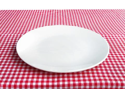 Empty white ceramic plate on table with red checkered tablecloth. Stock Photos
