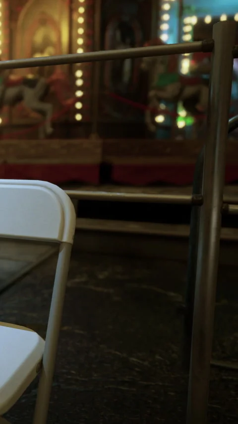 Empty white chair near a carousel in an amusement park setting Stock Footage 342127617