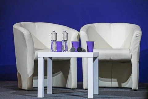 Empty white chairs with a table with water and cups before a conference Stock Photos