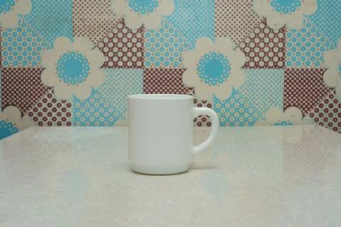 Empty white coffee mug on smooth table against colorful floral background Stock Photos