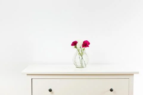 Empty white commode with three flowers on tablecloth. White wall with free sp Stock Photos