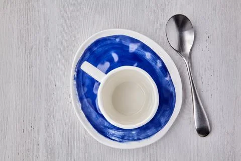 Empty white cup for hot drinks with a spoon on a blue plate on a white wooden Stock Photos