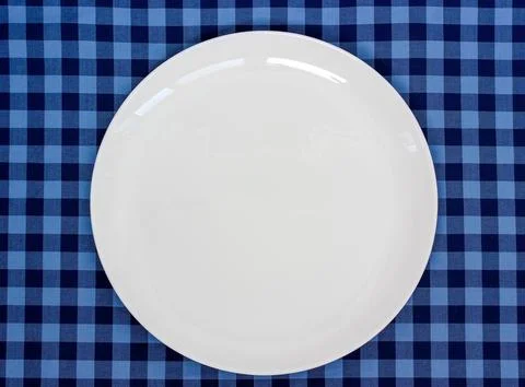 Empty white dinner plate resting on a blue checkered gingham tablecloth, pr.. Stock Photos