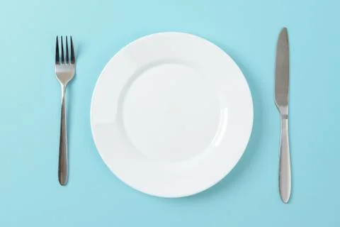 Empty white dinner plate, table knife and fork on a blue background. Set table Foto stock