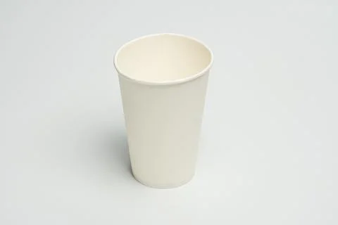 Empty white disposable cup on a light grey surface, cylindrical shape with no Photos
