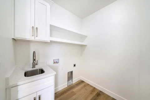 Empty white laundry room with top storage, laundry connections and dryer vent on Stock Photos