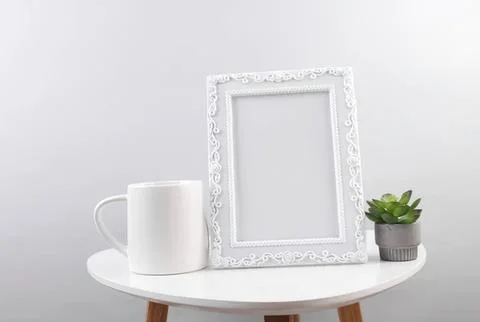 Empty white picture frame mug and plant on round table Stock Photos