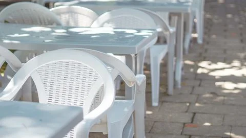 Empty white plastic chairs and tables on an outdoor cafe terrace. Stock Photos
