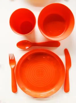 Empty white plastic plate, cup, fork and spoon over white background with copy Stock Photos