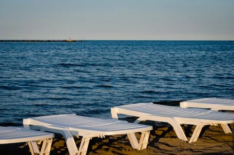 Empty white plastic sunbeds set on the seafront, during summer  season. Stock Photos