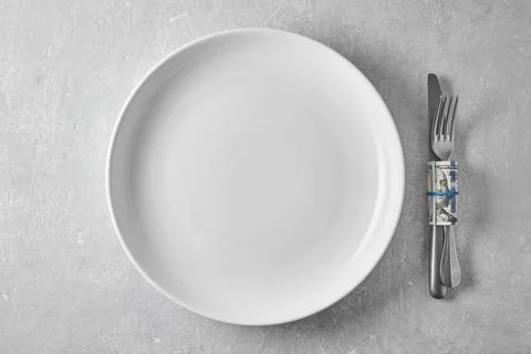 An empty white plate and a dinner fork and knife wrapped in a hundred dolla.. Stock Photos