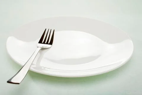Empty white plate and fork on pale green background Stock Photos