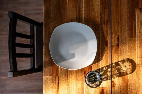 Empty white plate beside a glass. Sunlit wooden dining table from above. Stock Photos