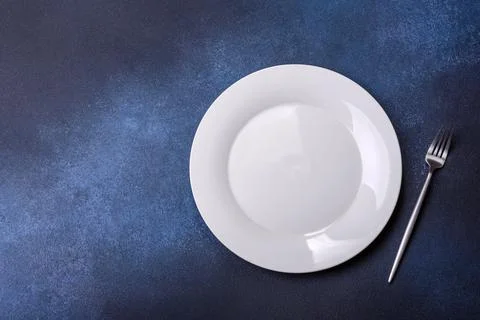 Empty white plate on blue background table. Flat lay Stock Photos