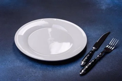 Empty white plate on blue background table. Flat lay Stock Photos