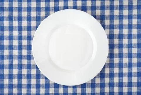 Empty white plate on checkered tablecloth. Stock Photos