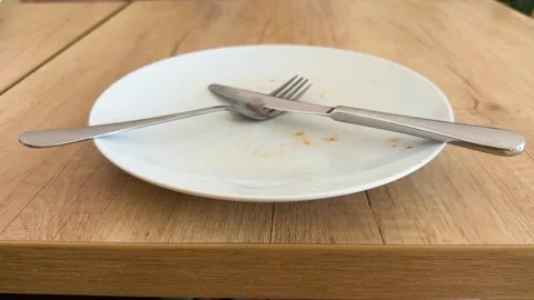 Empty white plate with crossed fork and knife on wooden table 스톡 동영상 343410718