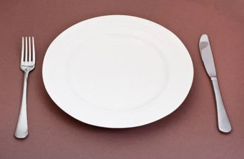 Empty white plate with fork and knife set on brown Foto stock