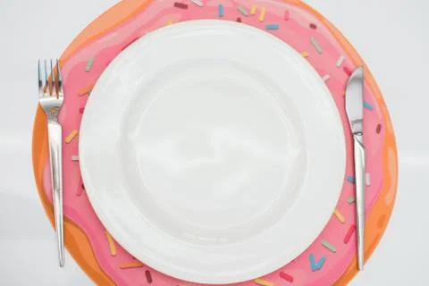 Empty white plate, fork and knife, on a donut rug, on a light background. Stock Photos