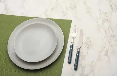 Empty white plate fork and knife on green and marble table 스톡 사진