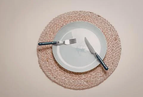 Empty white plate with fork and knife on a round placemat 스톡 사진