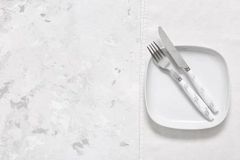 Empty white plate with fork and knife on linen napkin and textured concrete b Stock Photos