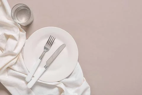 Empty white plate with fork and knife, glass of water, and linen napkin on ne Stock Photos