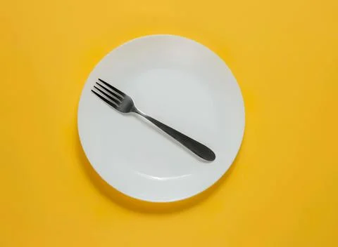 Empty white plate with fork on yellow background Foto stock