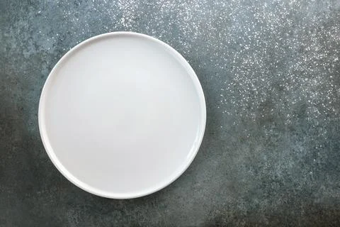 Empty white plate on a gray-blue background sprinkled with powder. Stock Photos