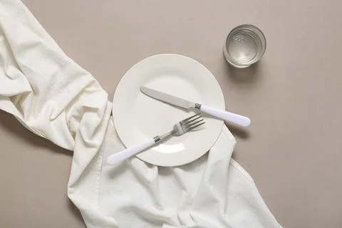 Empty white plate with silverware and water glass on neutral background with  Stock Photos