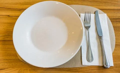 Empty white plate with spoon and knife on wooden background Stock Photos