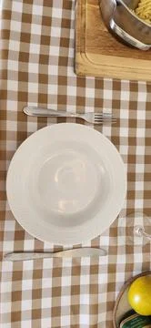 An empty white plate on a table with a checkered tablecloth Stock Photos
