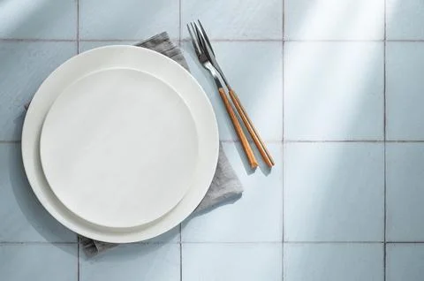 An empty white plates with a fork, knife and napkin on a blue tile background Stock Photos