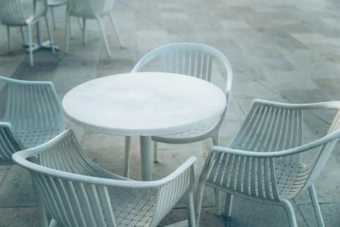 Empty white round table and plastic chairs set up on a stone terrace outsid.. Fotos Stock