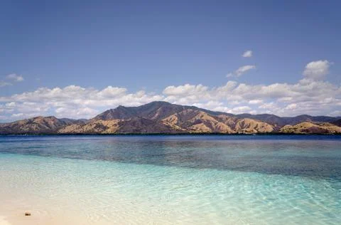 Empty white sand beach with calm blue ocean overlooking an island. Stock Photos
