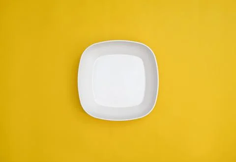 Empty white square plate isolated on yellow background Stock Photos