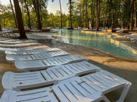 Empty white sunbeds by the pool in a lush green forest Stock Photos
