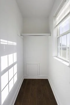 Empty White Walk-In Closet With A Window And Hardwood Flooring Inside. Stock Photos