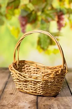 Empty wicker basket on rustic wooden table with blurred grape leaves for au.. Fotos Stock