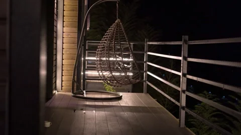 Empty wicker hanging swing chair swinging gently at night Video stock 345753046