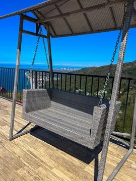 Empty wicker swing on deck with sea and city view, concept of relaxation, tra Foto stock