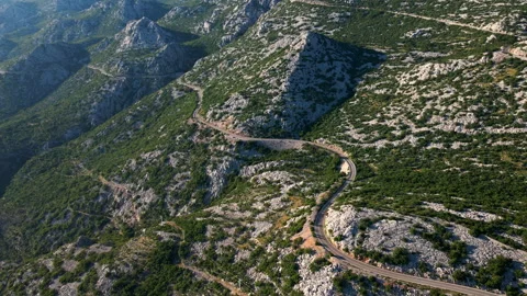 Empty winding mountain road through rugged rocky landscape from above Stock Footage 341278676